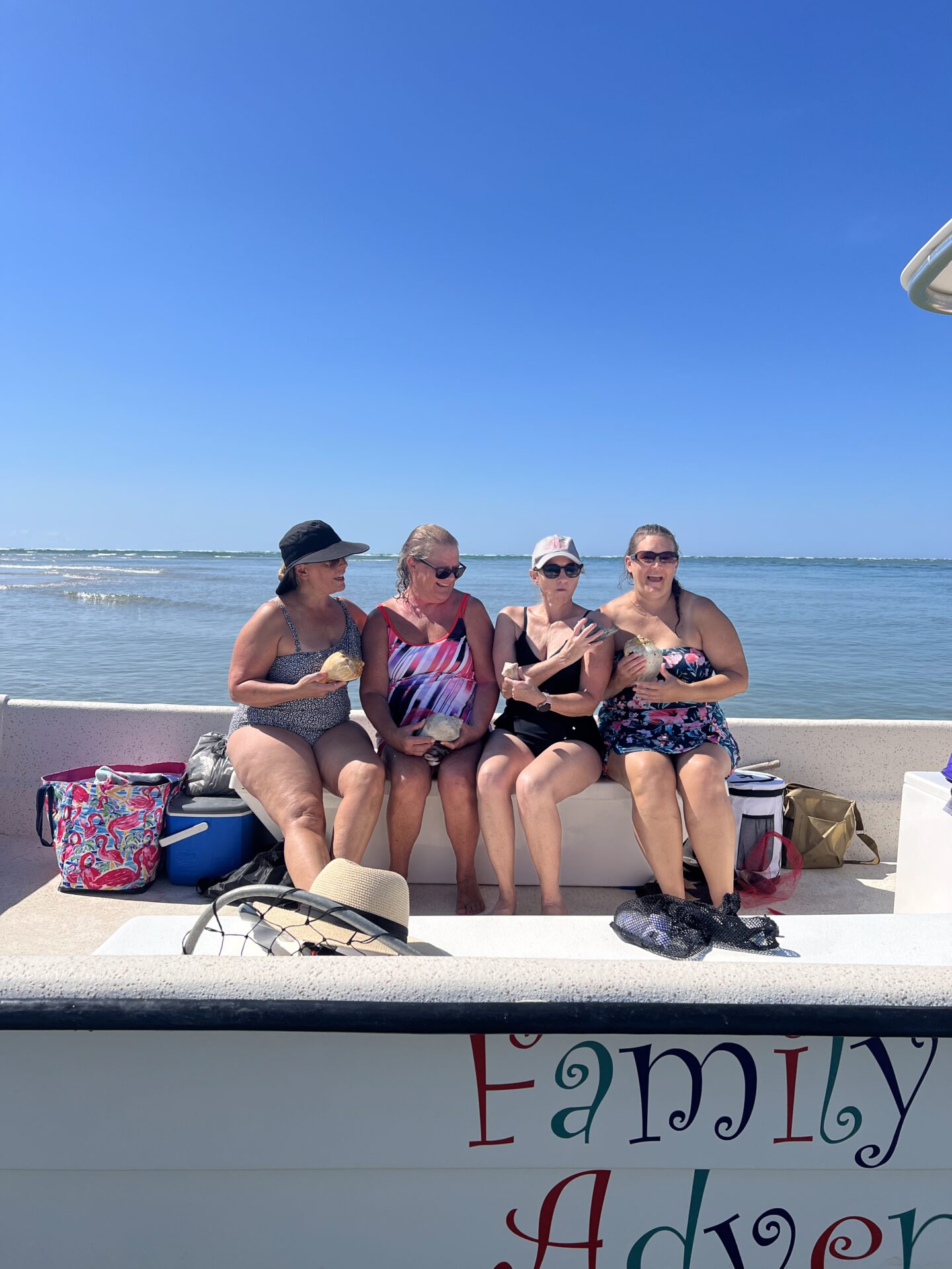 Four women sitting on a bench enjoying a sunny beach day.