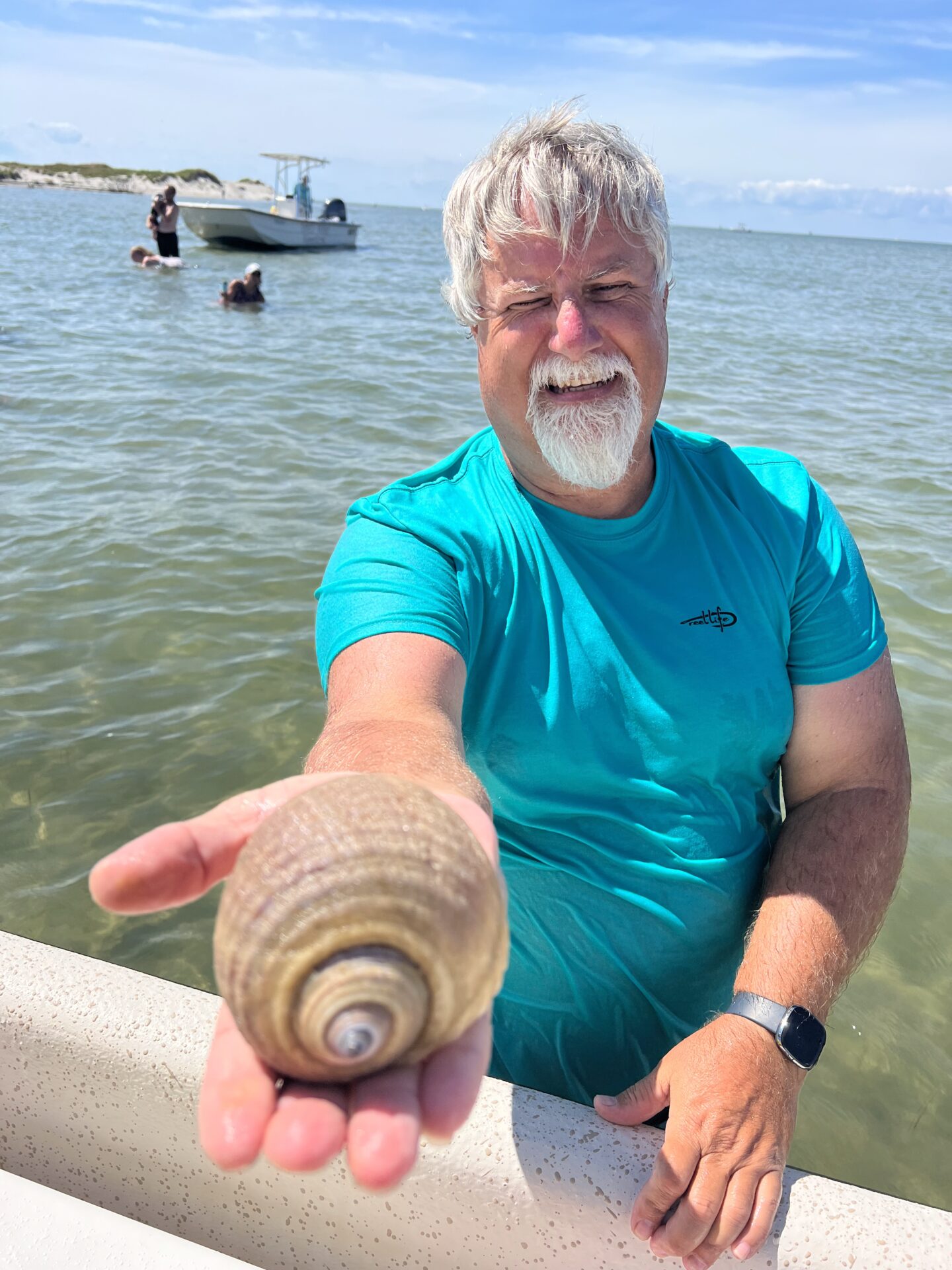 Man proudly displaying a seashell while sitting on a boat in the water.